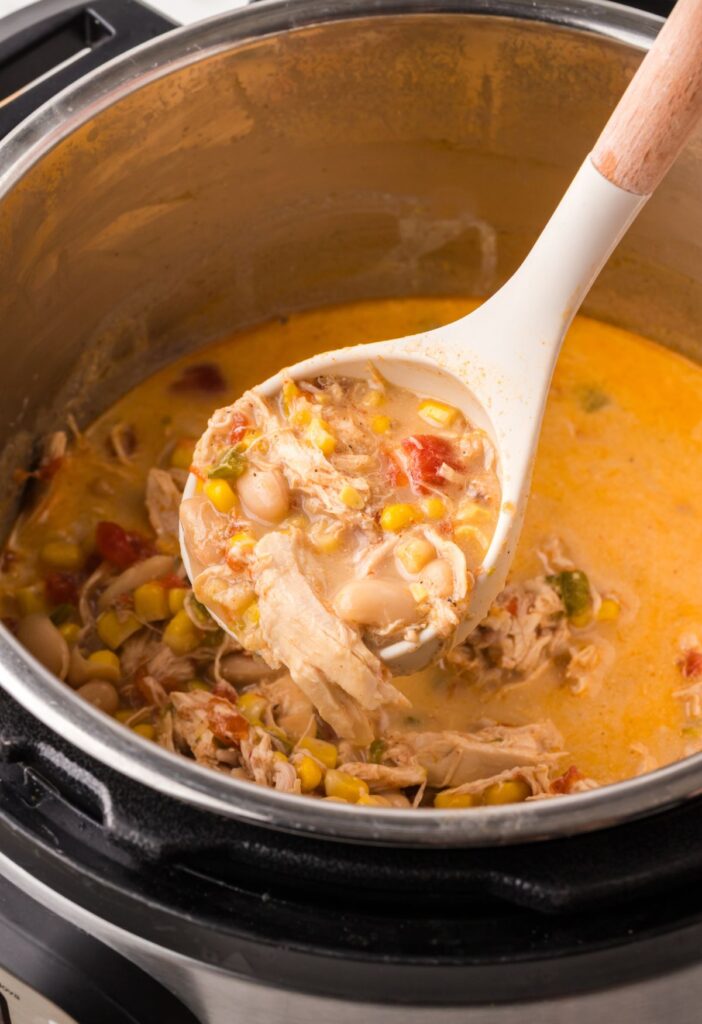 Inside of the instant pot showing the chicken chili, soup ladle holding some chili in it above the instant pot.