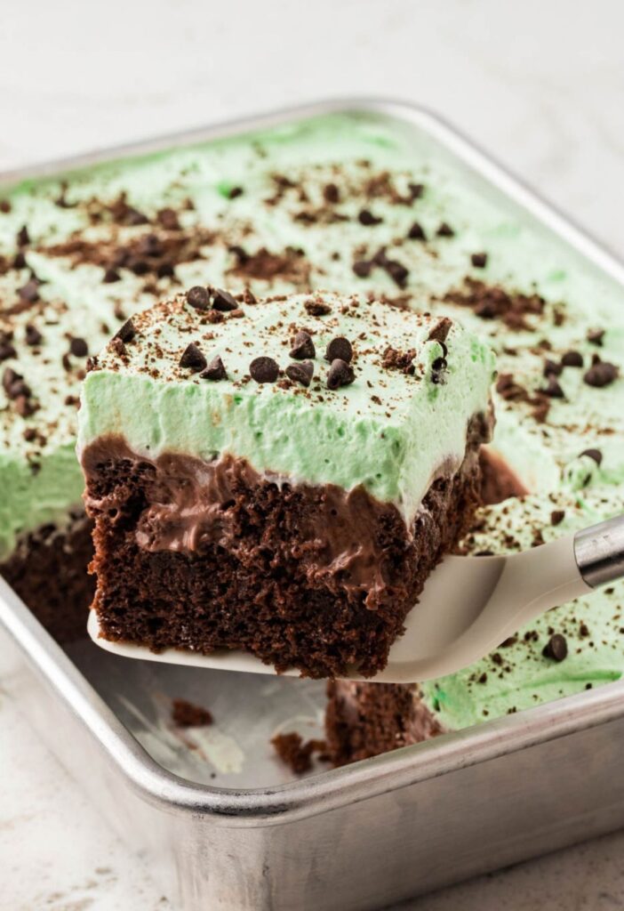 A spatula holding a piece of poke cake on it above the cake pan of cake.