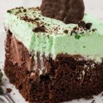 A slice of mint chocolate poke cake with a green mint whipped cream.