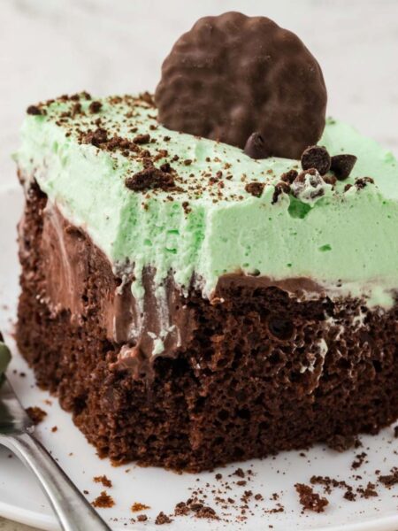 A slice of mint chocolate poke cake with a green mint whipped cream.