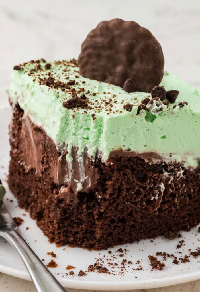 A slice of mint chocolate poke cake with a green mint whipped cream.