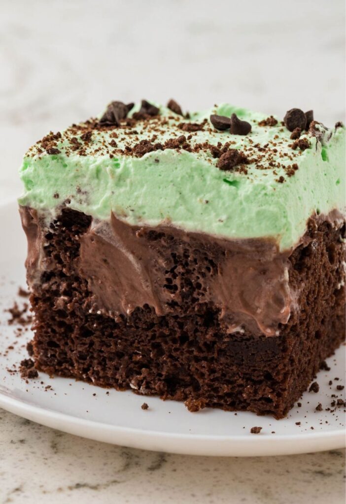 A piece of poke cake with mint whipped cream on a white plate.