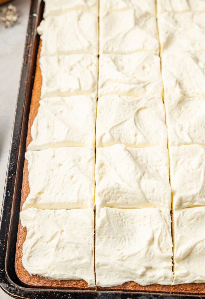 A tray of baked pumpkin bars frosted with a cream cheese frosting and cut into squares.