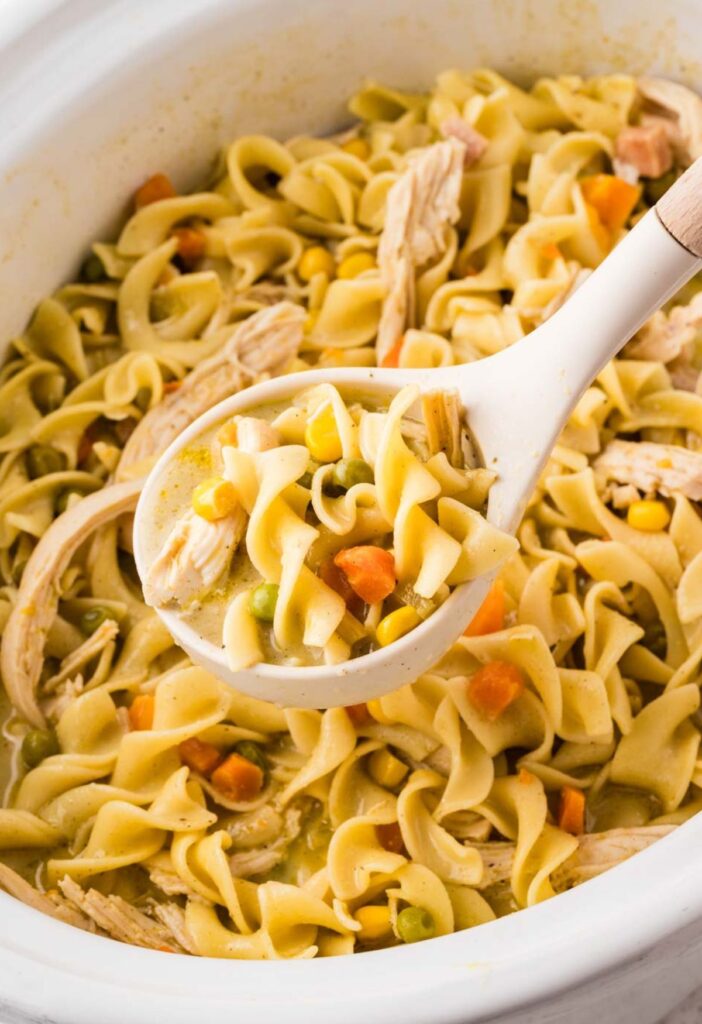 A ladle scooping up some of the pot pie noodles from inside the crockpot.