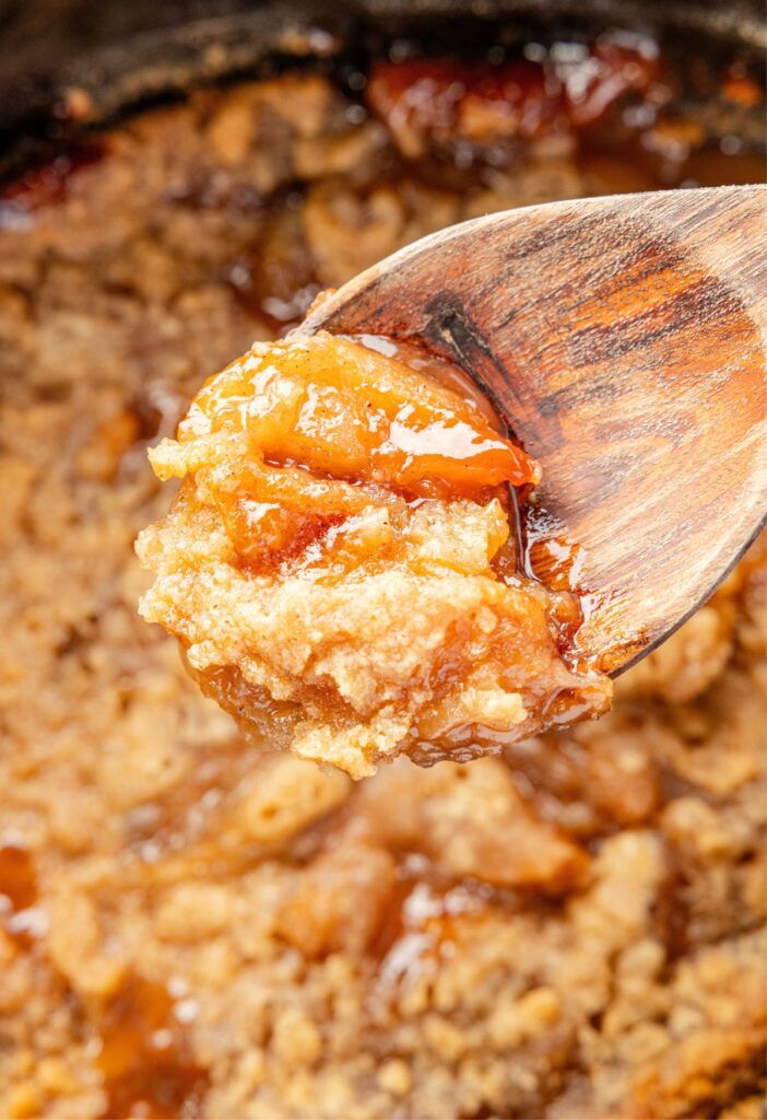 A wooden spoon scooping up some apple crumble from the crock pot.