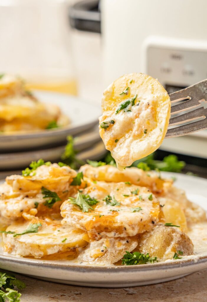 A fork holding a thinly sliced scalloped potato on it.